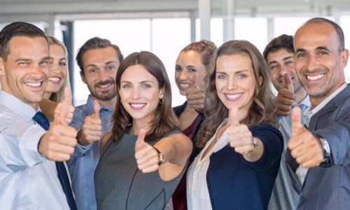 Group of happy business people showing sign of success. Successful business team showing thumbs up sign and looking at camera. Smiling businessmen and businesswomen cheering at office.